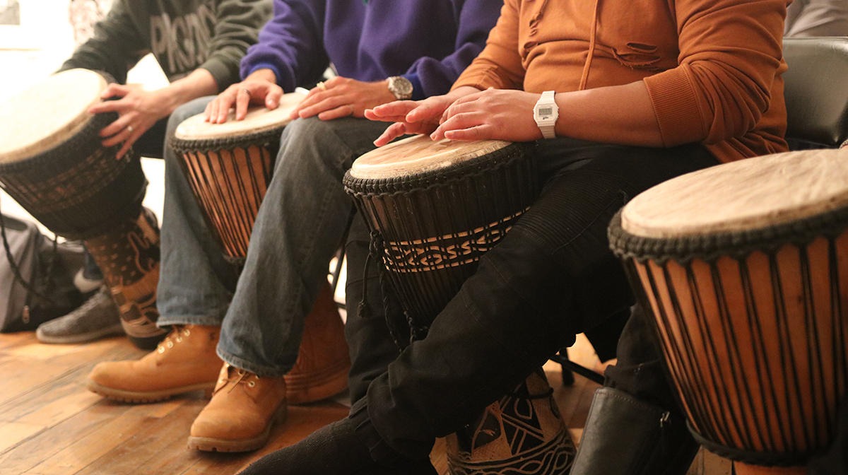 The hands of three men on djembe drums.